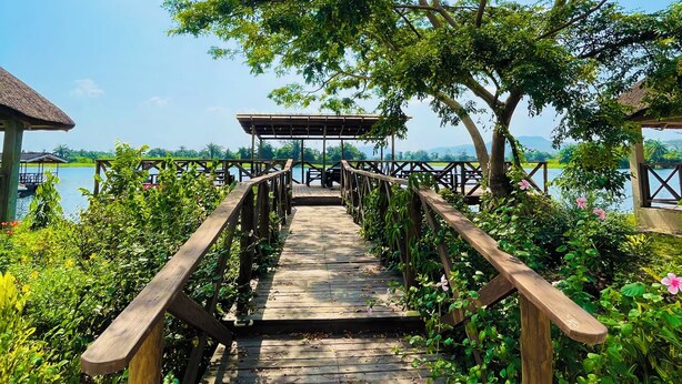 A wooden bridge leading to a wooden structure over water, surrounded by greenery. - Platinum Blue Island Resort (Akosombo)