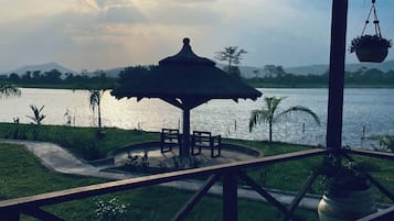 Un belvédère abritant une table et des chaises, d’où l’on peut admirer un plan d’eau, le tout étant entouré de verdure et surplombé par un ciel dégagé.