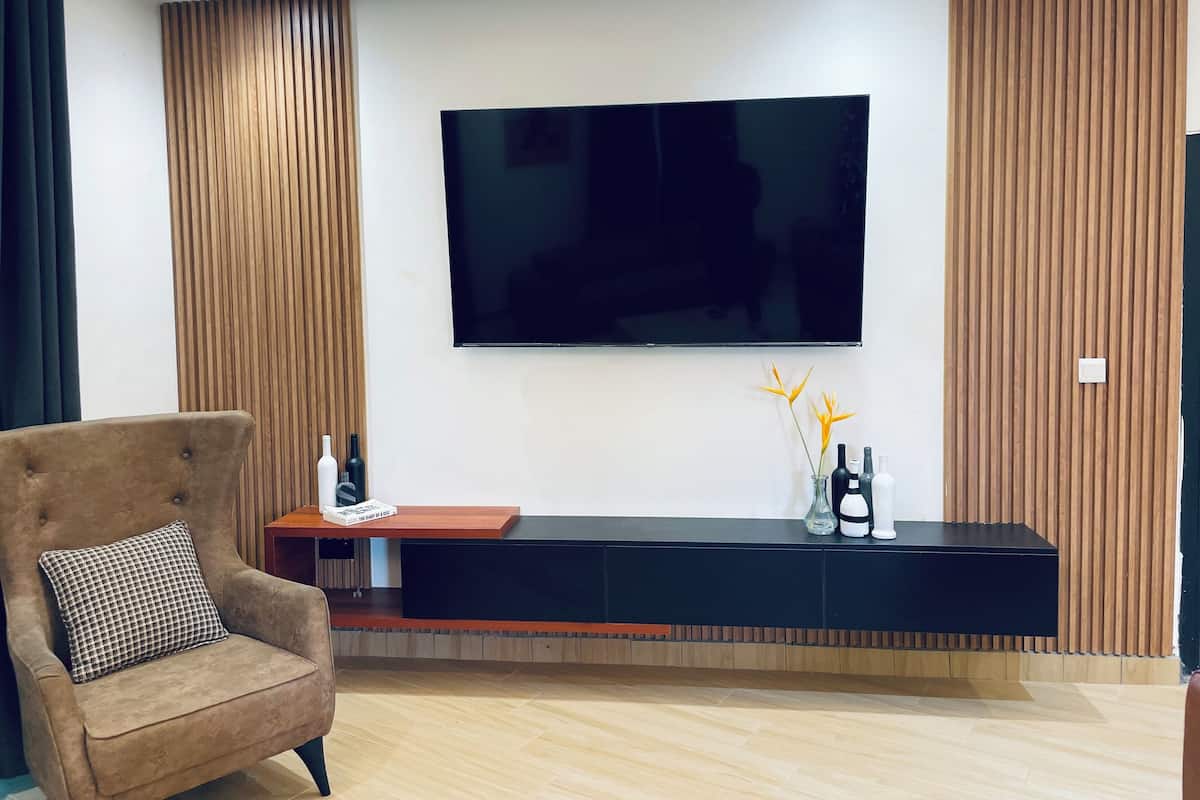 A modern living room with a flat-screen TV mounted on the wall, a wooden panel wall, a dark entertainment unit, and a plush armchair.