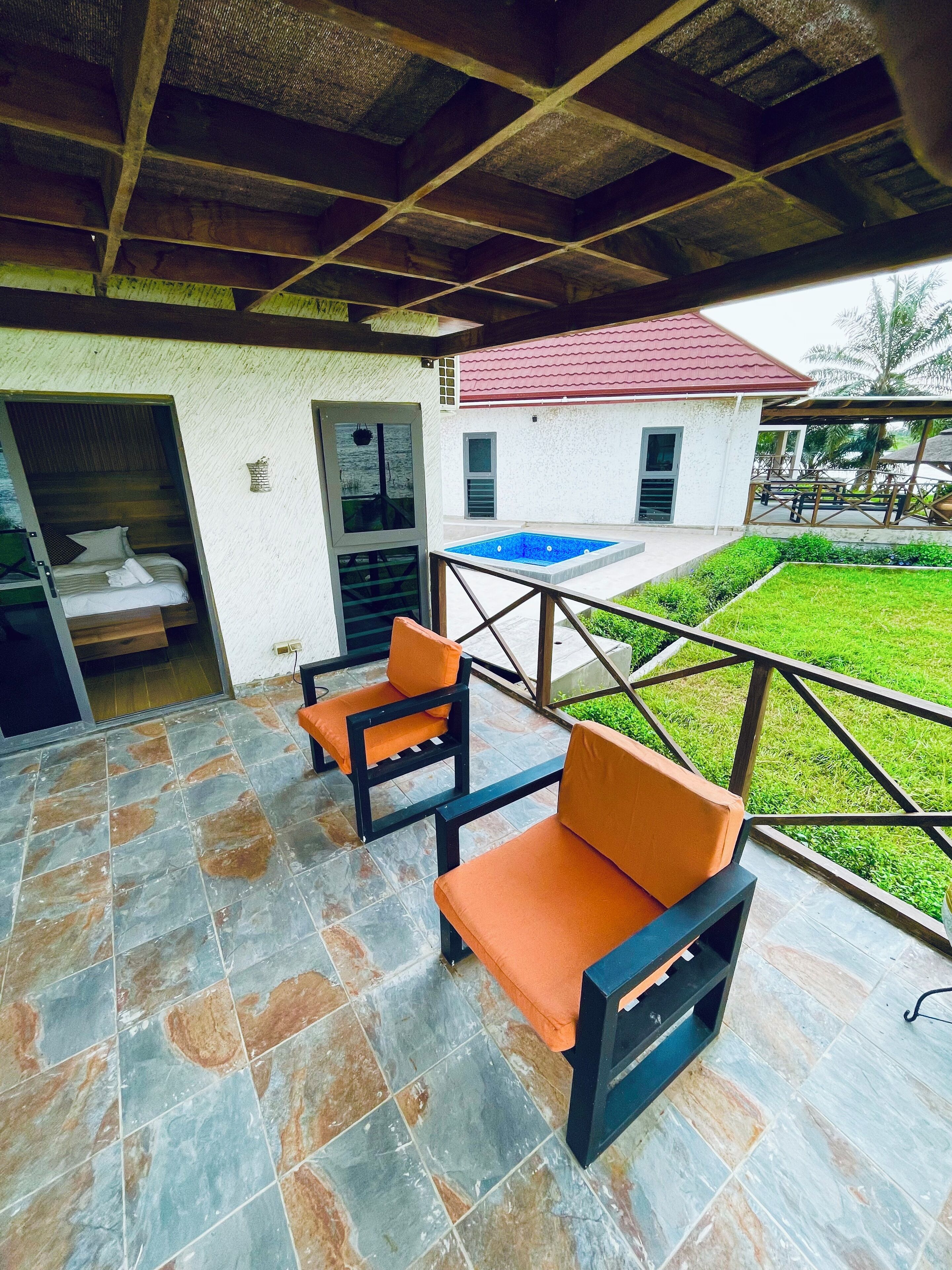 A covered patio area with stone flooring, two orange cushioned chairs, and a small pool.