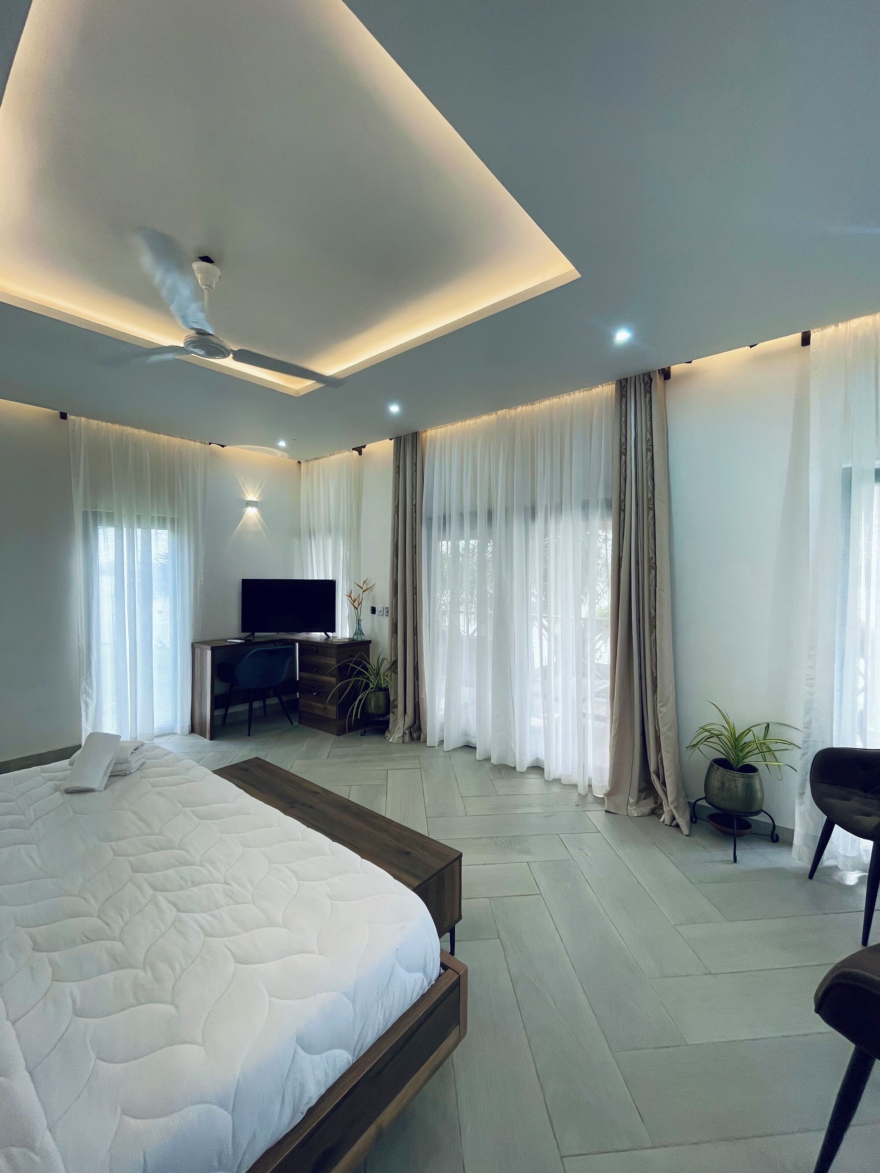 A modern bedroom with a large bed, a desk with a TV, and a ceiling fan.
