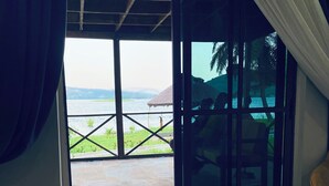 A room with a bed, a view of a body of water, and a patio area with a chair and umbrella. - Platinum Blue Island Resort (Akosombo)
