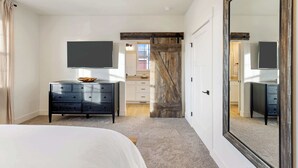 A bedroom with a large bed, a dresser, a TV mounted on the wall, and a sliding barn door. - Antler's Peak | Bridger Views & Close to Airport (Belgrade)