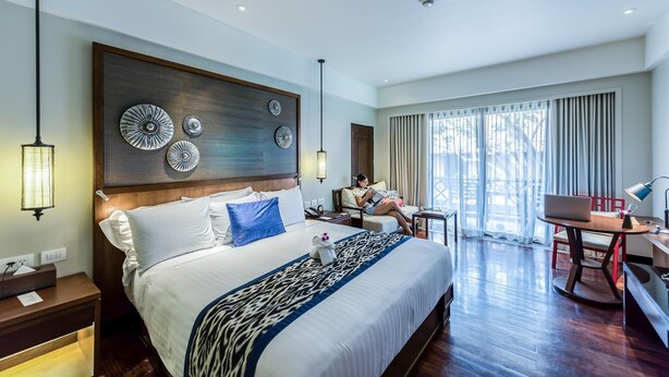 Ein Hotelzimmer mit einem großen Bett, einem Schreibtisch und einem Sessel. An der Wand über dem Bett befinden sich dekorative Teller.
