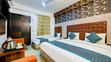 A hotel room with two beds, a wooden desk with a kettle and cups, and a ceiling fan.