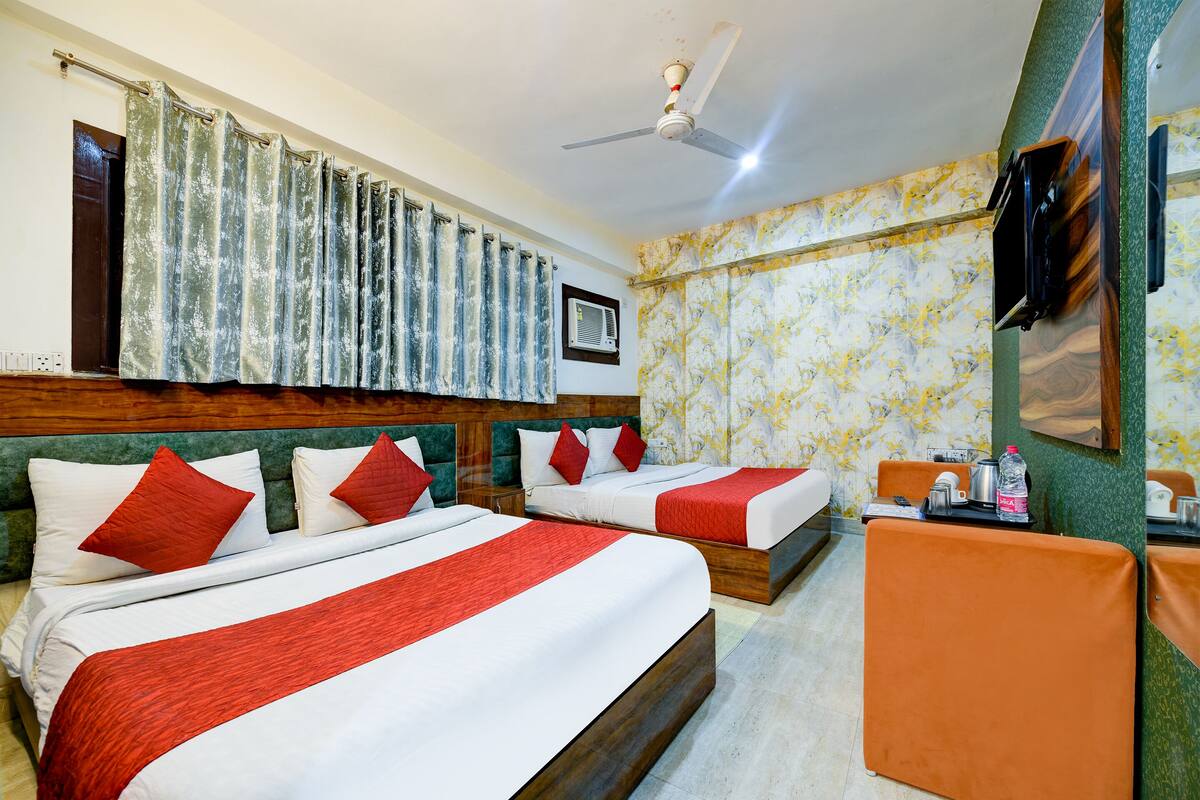 A hotel room with two beds, a ceiling fan, a TV, and a small table with a bottle and a cup.