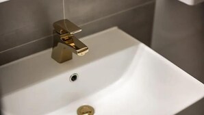 A white bathroom sink with a gold faucet and a drain. - Zavolle Hotel (Suwon)