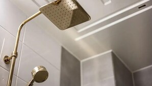 A showerhead with a square, perforated design, attached to a curved, metallic arm. - Zavolle Hotel (Suwon)
