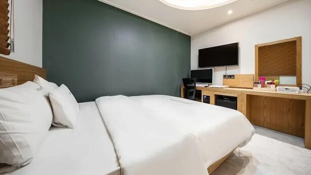 A modern hotel room with a large bed, a desk with a flat-screen TV, and a small kitchenette. - Zavolle Hotel (Suwon)