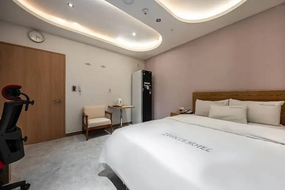 A hotel room with a bed, a desk, a chair, a clock, and a minibar.