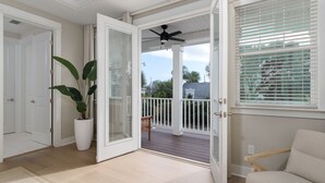 Une pièce dotée d’une porte-fenêtre coulissante donnant sur un espace extérieur abrité, équipé d’un ventilateur de plafond, d’une plante en pot et offrant une vue sur le quartier.