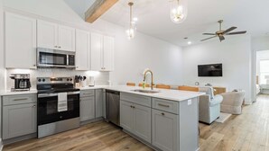 A modern kitchen with a built-in oven, microwave, and dishwasher, a large island with a sink, and a ceiling fan.