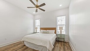 A bedroom with a wooden floor, a bed with white bedding, a ceiling fan, and two bedside tables with lamps.