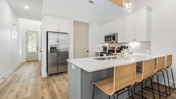 A modern kitchen with a central island, stainless steel appliances, and a dining area with wicker chairs.