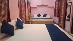A bedroom with two beds, a nightstand, and a potted plant. - Madhavi Homestay (Varanasi)