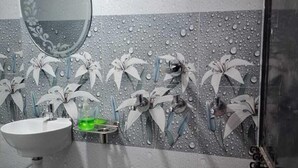 A bathroom with a sink, mirror, and a wall with a floral tile design. - Madhavi Homestay (Varanasi)