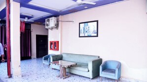 A room with a blue sofa, a small table, a blue armchair, a ceiling fan, and a framed picture on the wall. - Hotel Shree Mahalaxmi (Karchana)