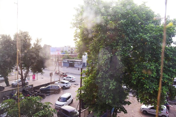 A parking lot with several cars and motorcycles, surrounded by trees and buildings. - Hotel Shree Mahalaxmi (Karchana)