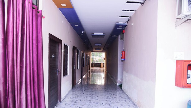 A corridor with a tiled floor, doors on the left, and a fire extinguisher on the right. - Hotel Shree Mahalaxmi (Karchana)