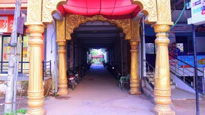 A covered walkway with ornate golden pillars and a red canopy, leading to a building entrance. - Hotel Shree Mahalaxmi (Karchana)