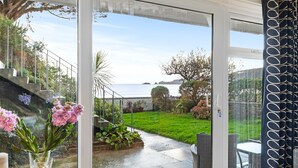 On aperçoit, à travers une porte vitrée, un jardin avec un espace patio, une table et des chaises.