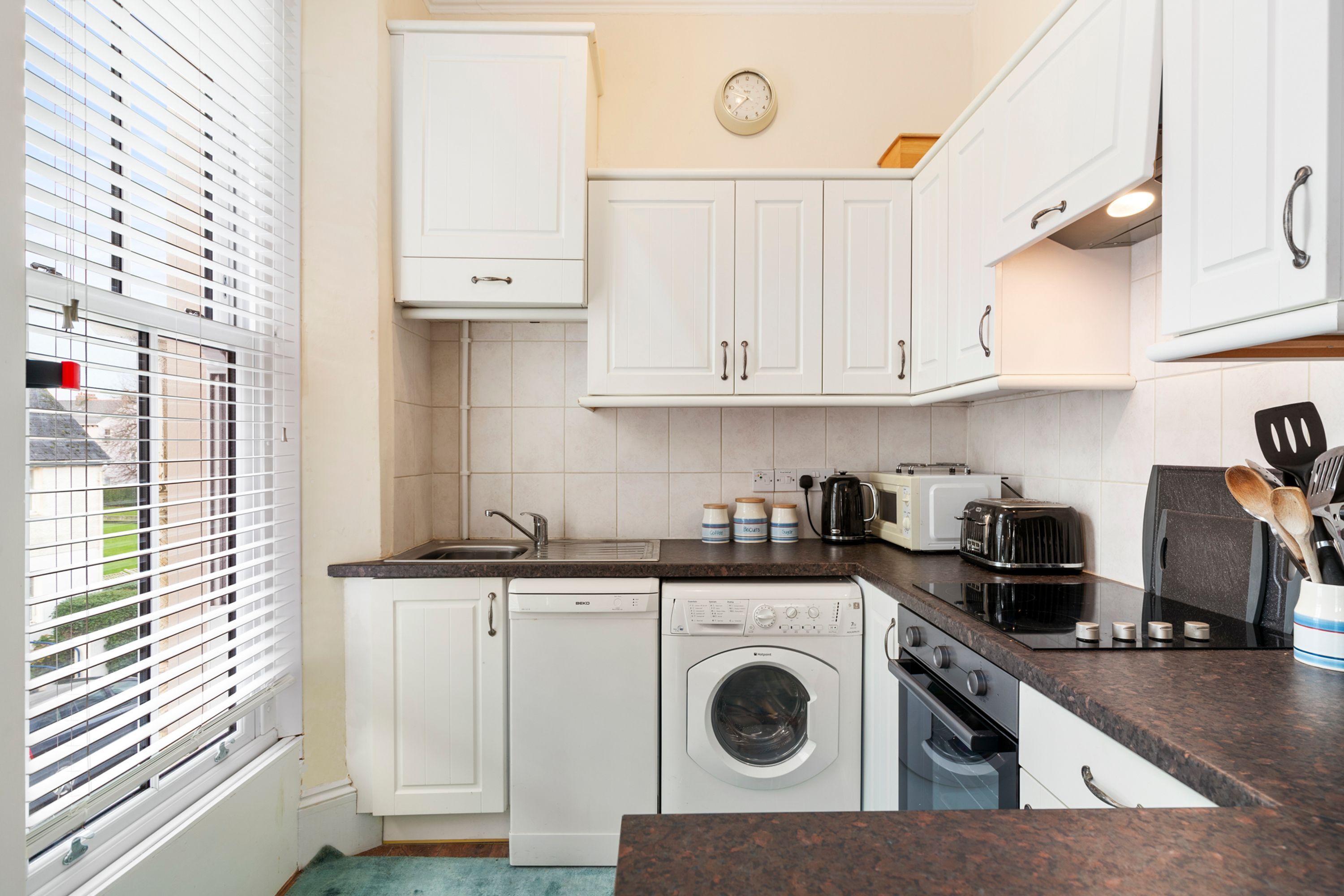 A kitchen with white cabinets, a washing machine, a toaster, and a sink.