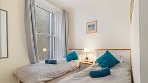 Een hotelkamer met twee bedden, een raam, een nachtkastje met een lamp en een ingelijste foto aan de muur.