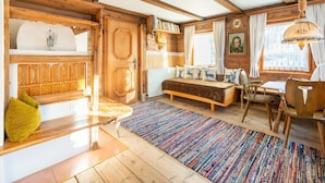 Ein gemütlicher, rustikaler Raum mit Holzbalkendecke, einem großen Bett mit gemusterten Kissen, einem farbenfrohen Teppich und einer hölzernen Bank.