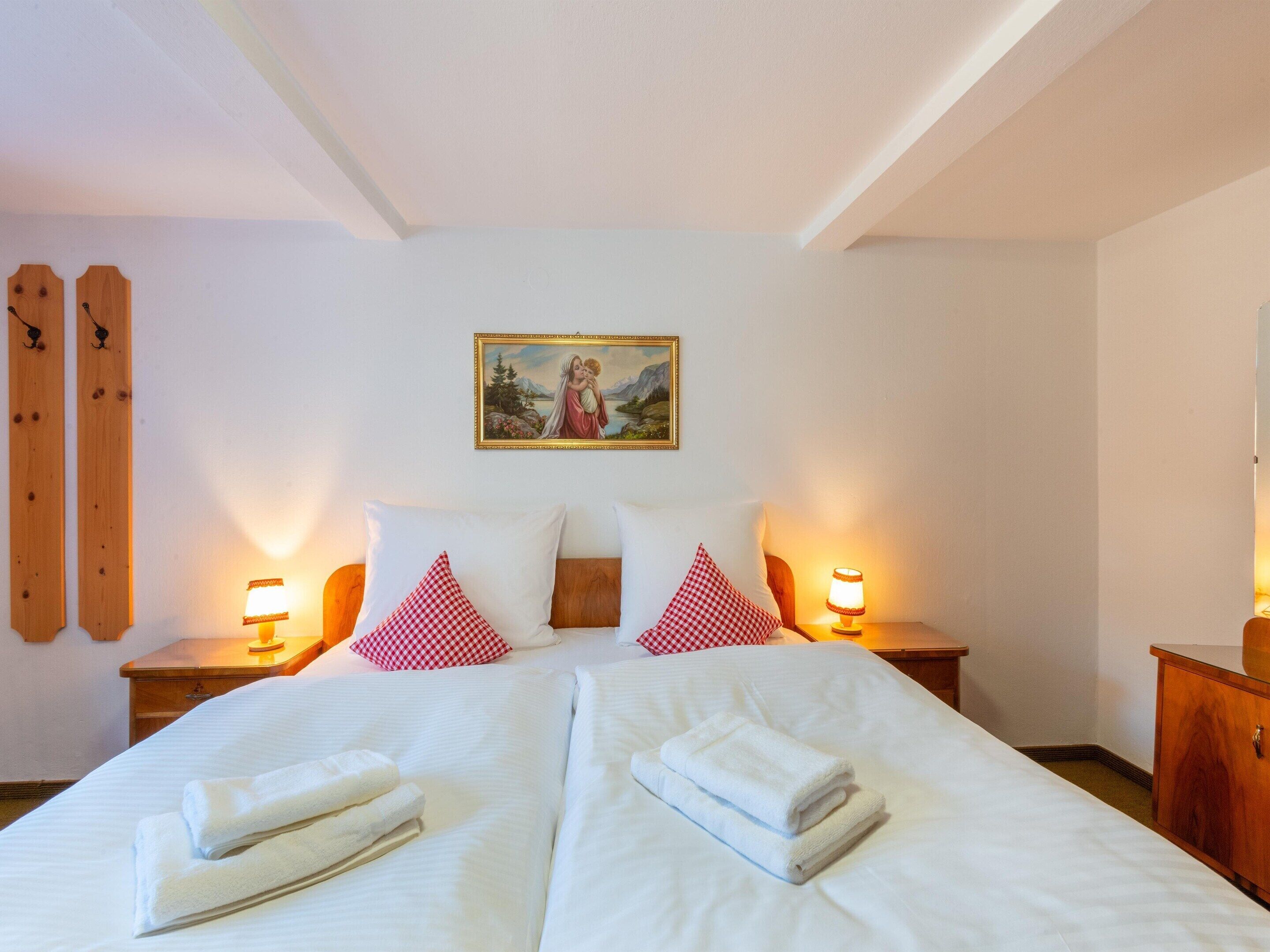 Habitación de hotel con una cama grande, dos mesitas de noche con lámparas, un cuadro en la pared y esquíes de madera apoyados contra la pared.