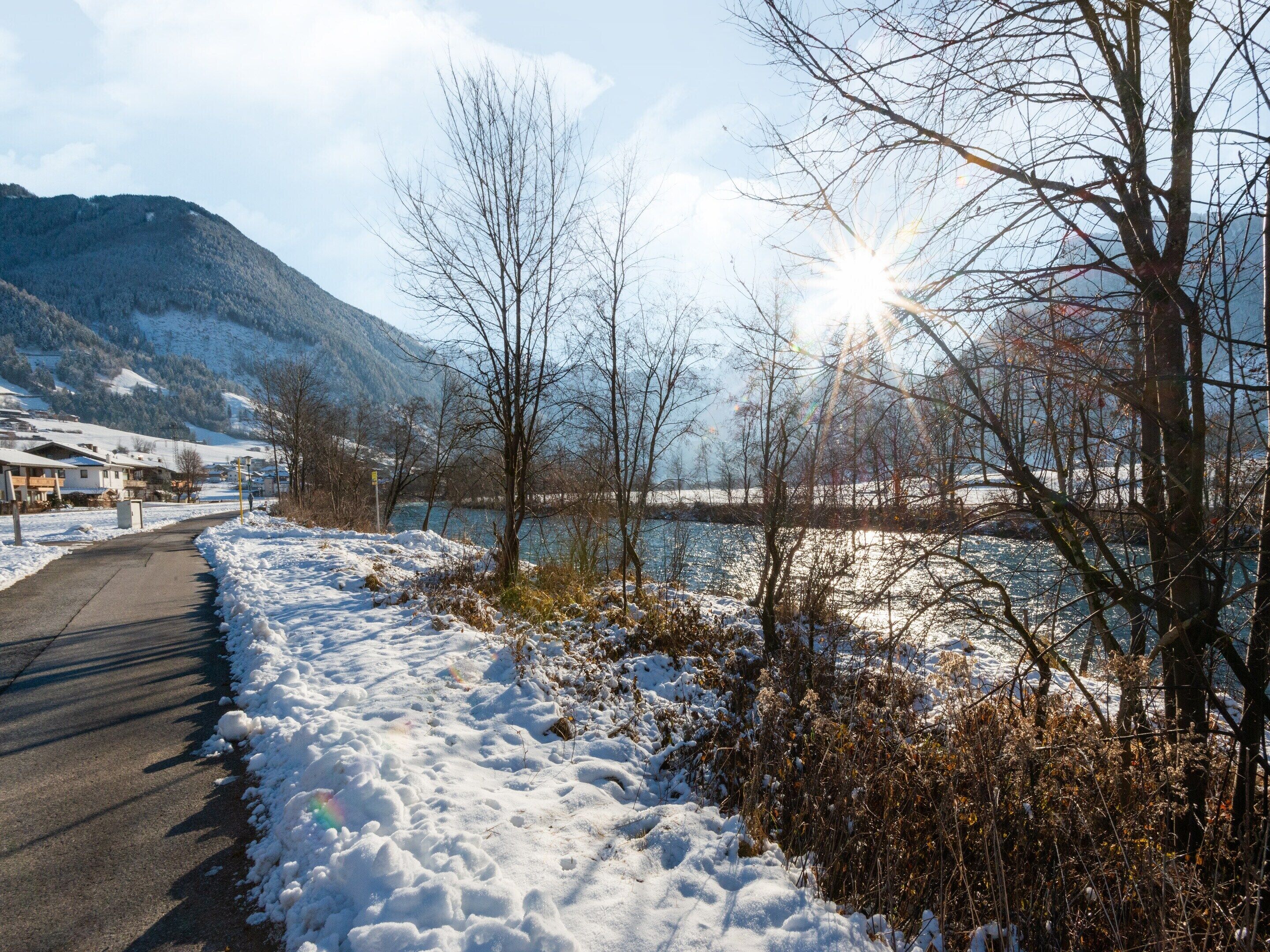 Un sentier enneigé longe un lac, avec des montagnes en arrière-plan.