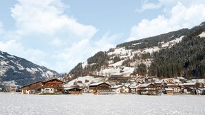 Ein verschneites Dorf mit traditionellen Holzhäusern, einem Berg im Hintergrund und einem klaren Himmel.