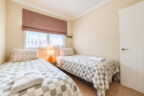 Ein Doppelzimmer mit zwei Betten, einem Fenster mit Vorhängen, einer Nachttischlampe und einer Tür.
