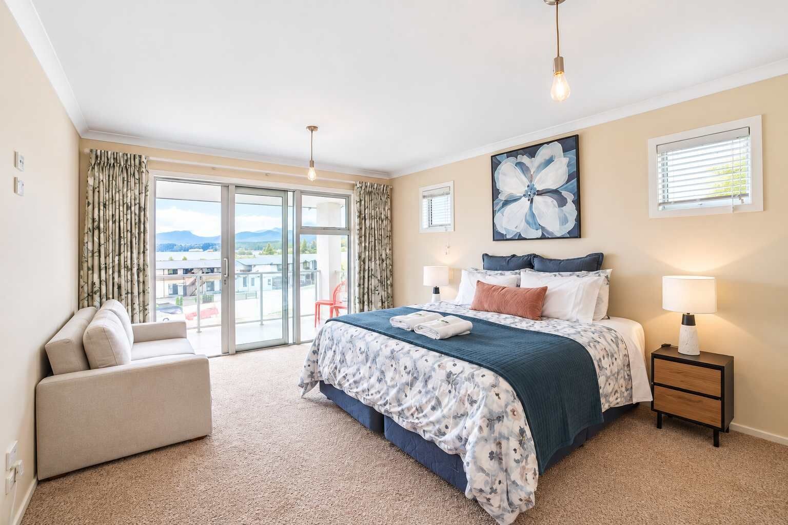 A hotel room with a large bed, a sofa, a balcony with a view, and a painting on the wall.