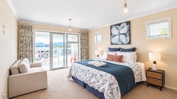 A hotel room with a large bed, a sofa, a balcony with a view, and a painting on the wall.