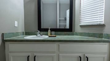 A bathroom with a white sink, a mirror, and a window with blinds.