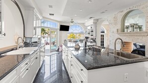 Una cocina amplia con una isla grande, armarios blancos y vista al exterior.