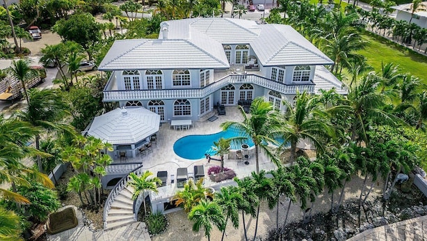 Una casa grande con piscina, rodeada de palmeras.