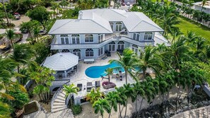 A large house with a swimming pool, surrounded by palm trees.