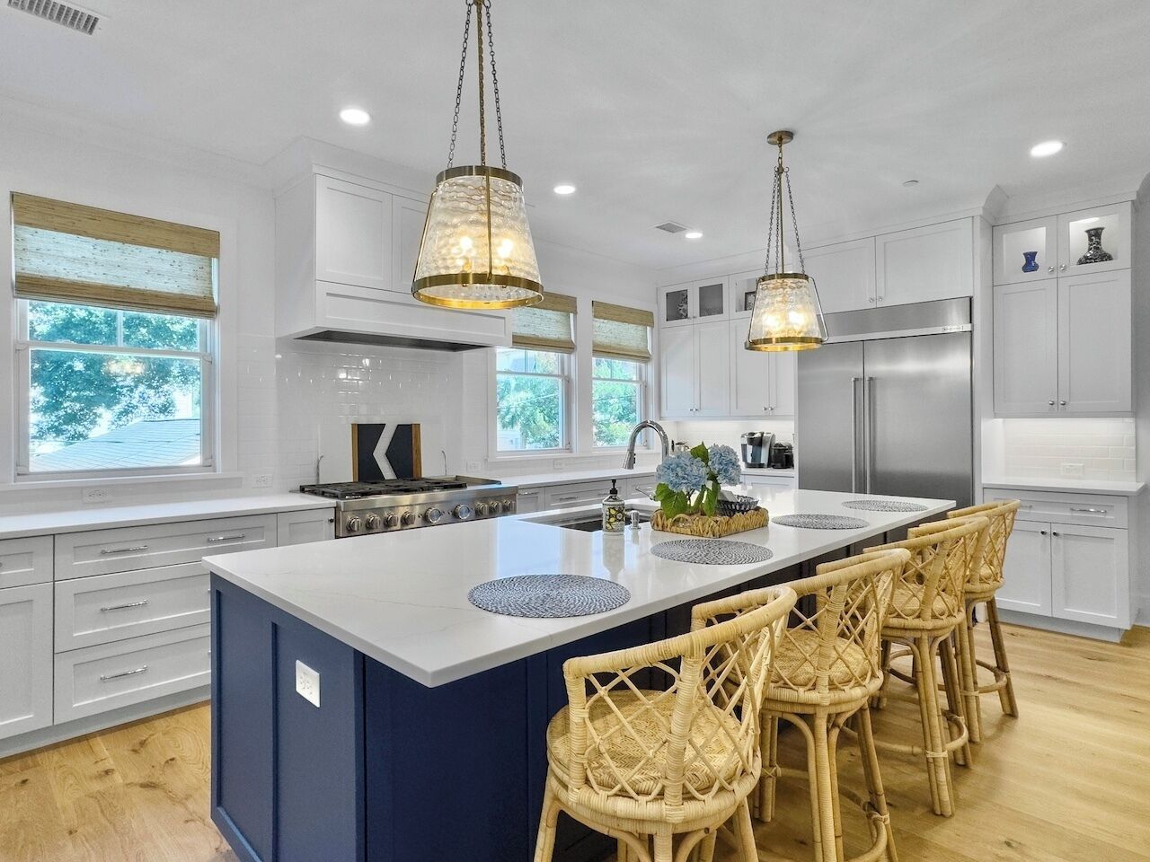 A modern kitchen with a large island, white cabinetry, and a stainless steel refrigerator.