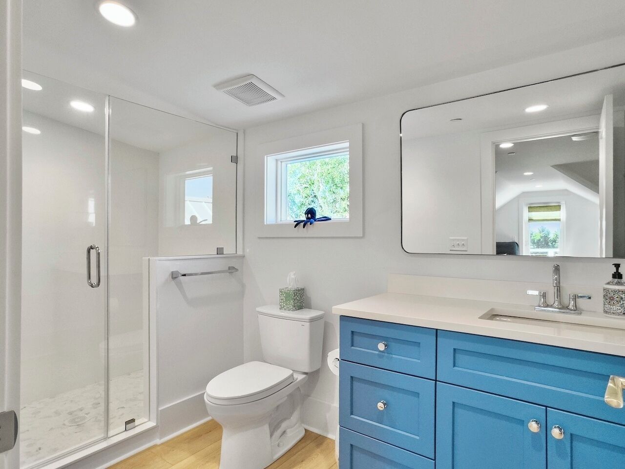 A modern bathroom with a glass shower enclosure, a white toilet, and a blue vanity with a mirror.