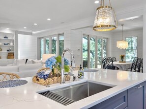 A modern kitchen with a large island, white cabinetry, and a dining area with a table and chairs. - 6 BR Home w/ Pool Close to Ocean | Chef's Kitchen (Isle of Palms)