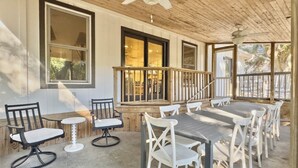 An outdoor patio area with a long table and multiple chairs, a ceiling fan, and large windows. - 4 BR Beach House w/ Lush Backyard | Pet Friendly (Isle of Palms)