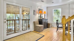 A spacious room with a wooden floor, a gray sofa, a dining table with chairs, a cabinet, and a staircase. - 4 BR Beach House w/ Lush Backyard | Pet Friendly (Isle of Palms)
