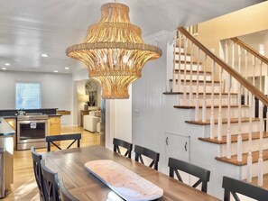 A modern kitchen with a dining area, wooden staircase, and pendant lighting. - 4 BR Beach House w/ Lush Backyard | Pet Friendly (Isle of Palms)