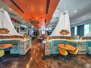 Un restaurant moderne avec des banquettes et des tables rondes, doté d’un bar central et offrant une vue sur la ville.