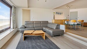 Ein modernes Wohnzimmer mit einer Eckcouch, einem Holztisch und einem Essbereich mit gelben Stühlen.