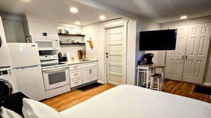 A bedroom with a large bed, a kitchenette with a microwave, oven, and refrigerator, and a TV mounted on the wall. - Charming Historic Studio Cottage (Lakeland)