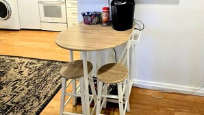 A compact kitchen with a washing machine, microwave, and coffee maker. There is a small round table with two stools and a TV mounted on the wall. - Charming Historic Studio Cottage (Lakeland)