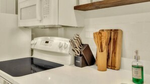A kitchen with a stove, microwave, wooden cutting board, knife block, and dish soap. - Charming Historic Studio Cottage (Lakeland)