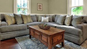 Ein Wohnzimmer mit einem grauen Ecksofa, einem Holztisch und einem gemusterten Teppich.